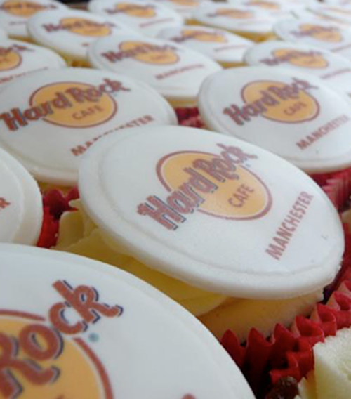 cupcakes with red cases and vanilla buttercream topped with a white fondant disc and decorated with an edible hard rock cafe logo