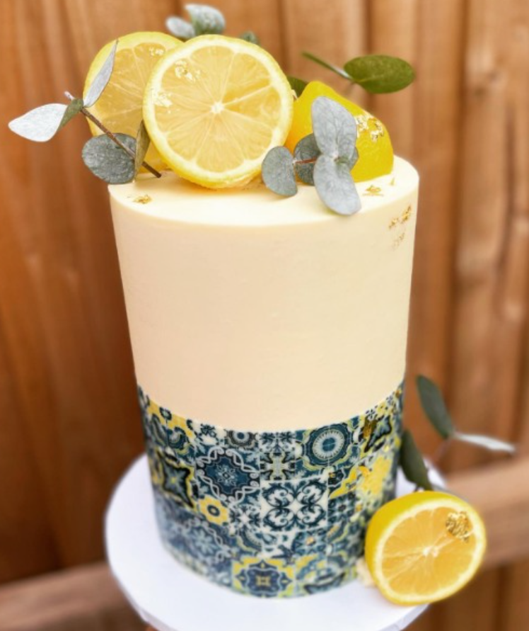 Tall cake featuring fresh lemons and foliage. An edible cake wrap wraps the lower half of the cake in a tile design.