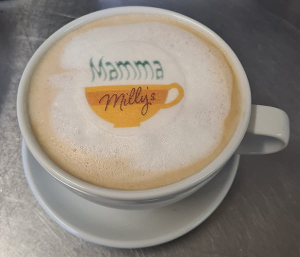 Coffee shop mug at mamma Milly's with a foamed milk top, adorning the coffee is the company's logo printed to edible wafer paper