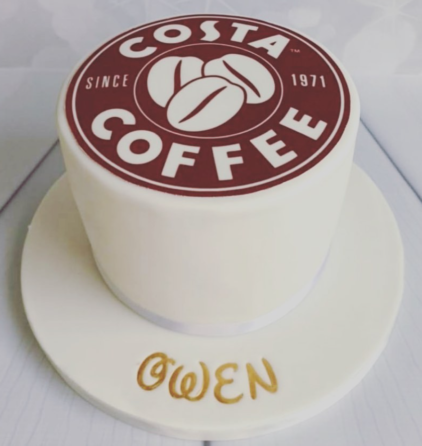 White fondant iced cake with a edible image on top of the costa logo. In gold lettering it says Owen on the board.