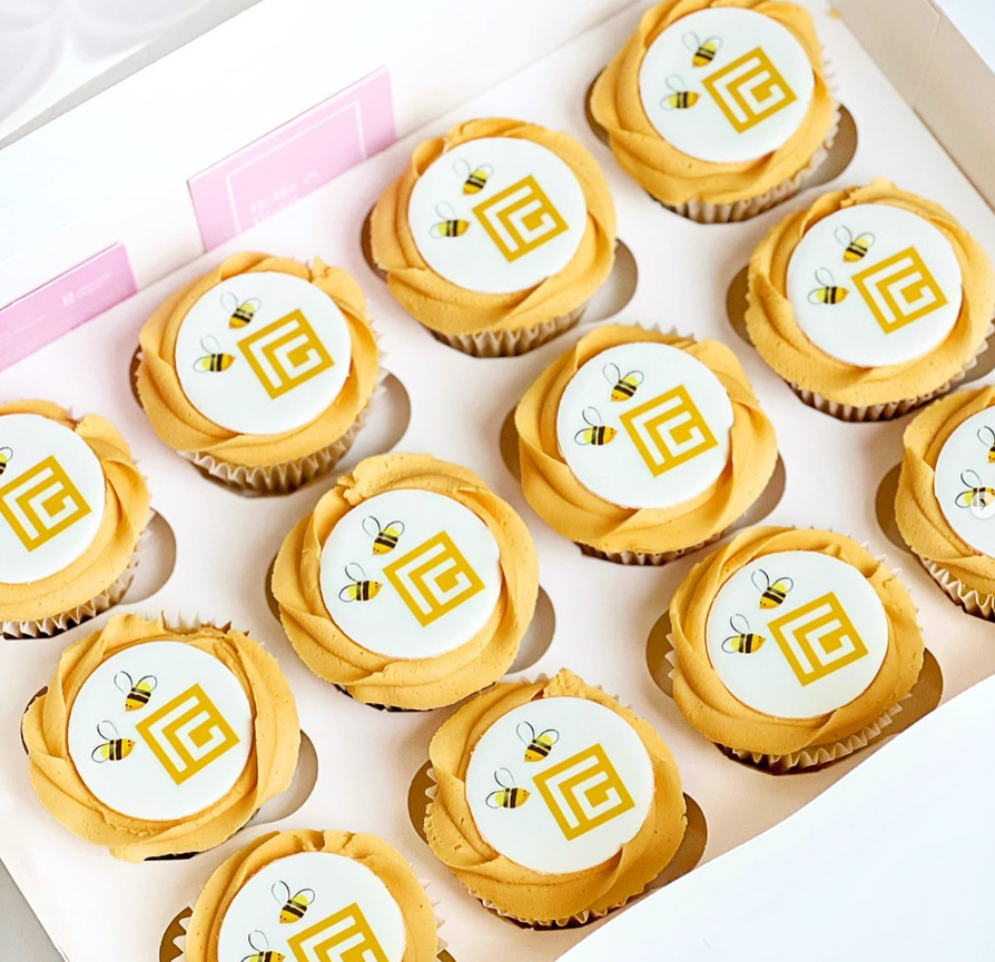 Lemon cupcakes with yellow swirl icing topped with edible  cupcake toppers. The icing is printed with a bee company logo
