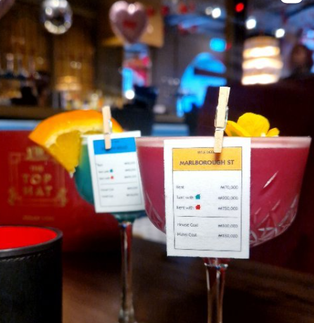 cocktails from life sized monopoly, one red and one blue. Each have an edible wafer card attached to the glass with a wooden peg
