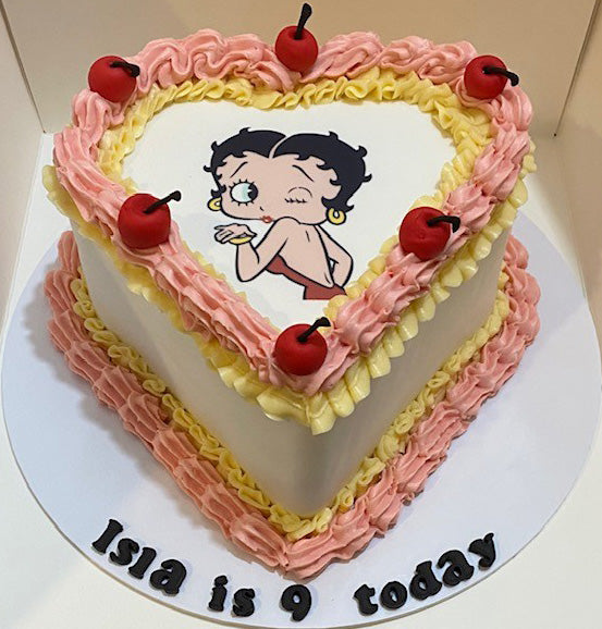 heart shaped cake with an edible image of betty boo for a birthday cake. Decorated with yellow and pink icing and fondant cherries
