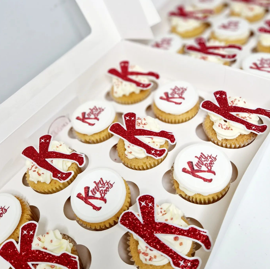 vanilla cupcakes with ivory buttercream topped with edible images featuring the theatre show, kinky boots. The edible prints are the logo and famous boots in glitter theme