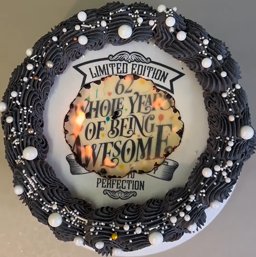 Birthday cake featuring a burn away cake topper, the cake has black piped buttercream, topped with a wafer image alight with another icing cake topper underneath