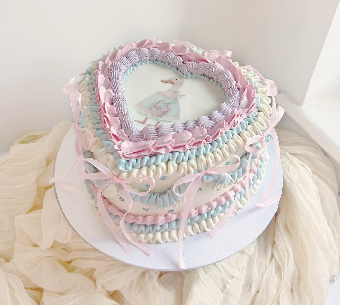 jemima puddleduck themed heart shape cake with pastel coloured piping and an edible print on top. Finished with some pretty pink bows