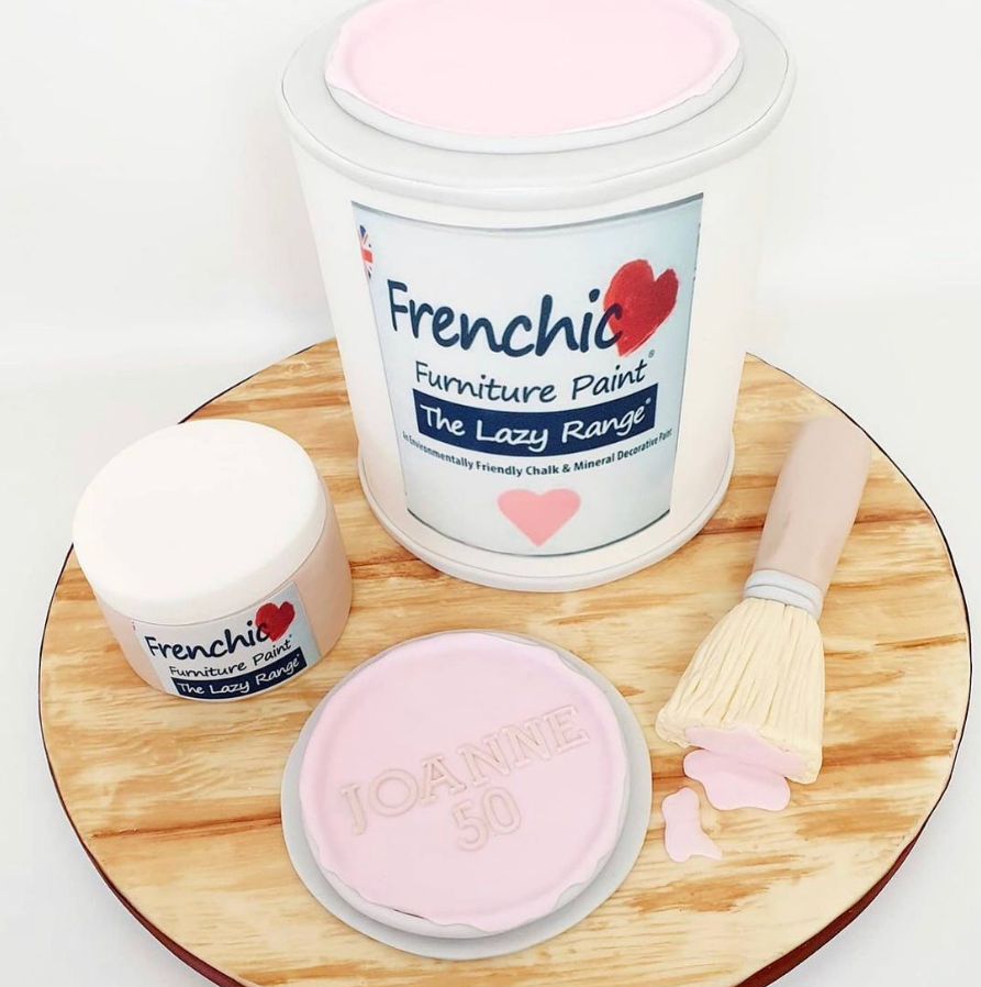 Cake in the shape of a Frenchic paint pot with a smaller pot and a paint brush. The pots have edible printed icing sheets of the pot labels. The cake board has a wooden effect.