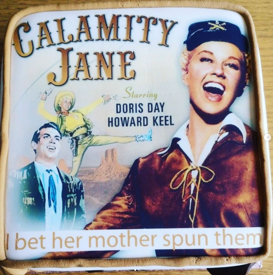 Square cake topped with a printed icing sheet of Calamity Jane poster cover with a personalised message. The top of the cake is bordered with a rope of brown icing.