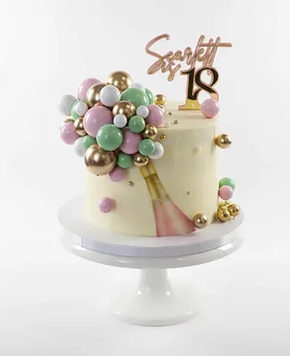 A frosted birthday cake on a white pedestal stand, decorated with pastel pink, green, and white balloon-like spheres, gold accents, rose gold champagne edible icing sheet and a gold 'Sarah 18' topper on a white background.